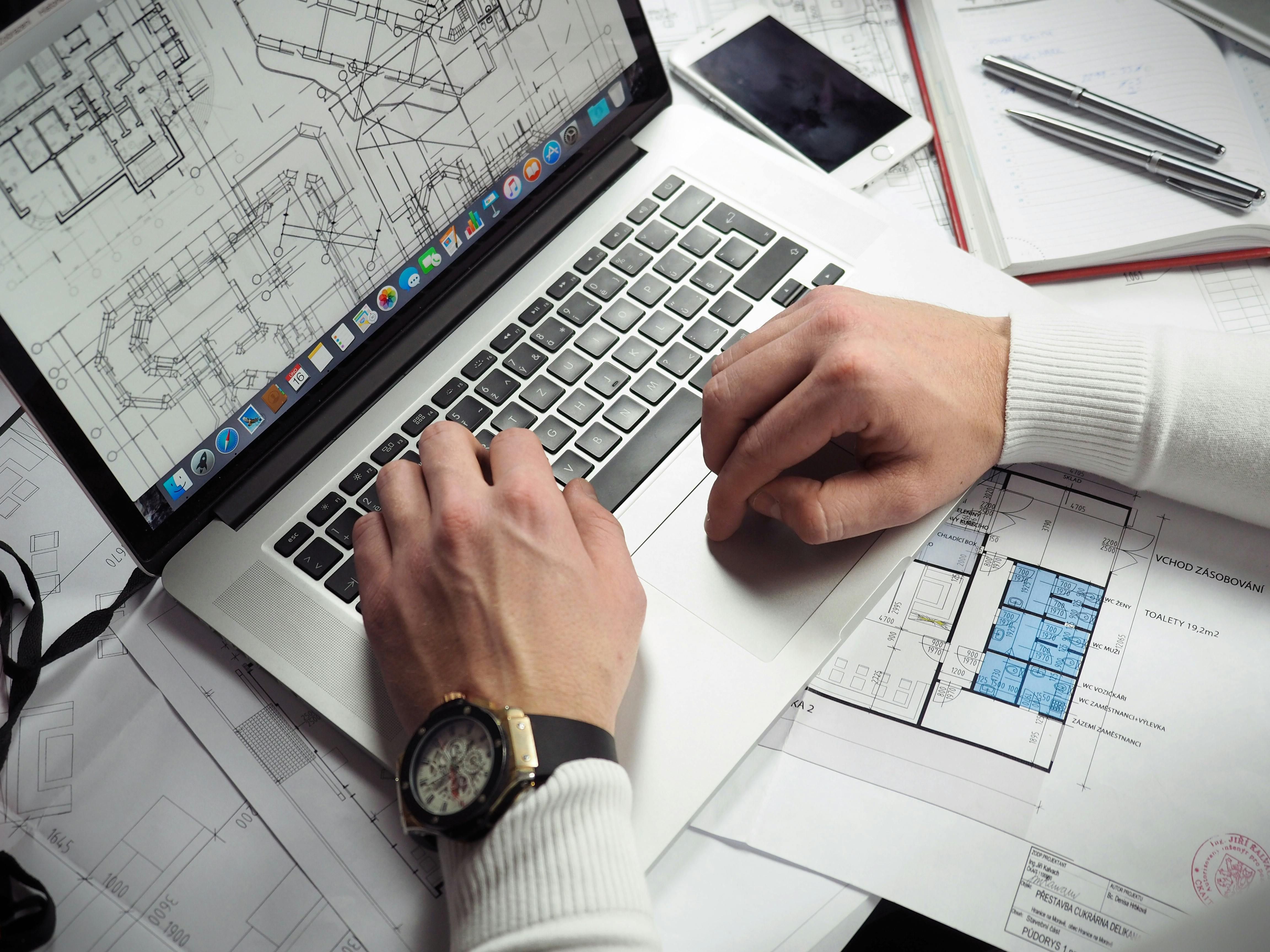 An individual with lots drawings and applications, working at their laptop